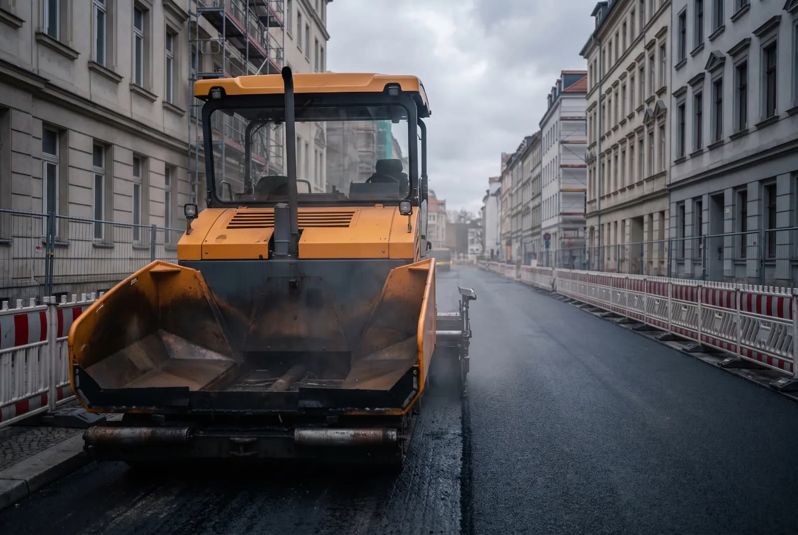 Asphaltfertiger steht nach Feierabend auf einer abgesperrten Berliner Wohnstraße vor der frisch eingebauten Decke.